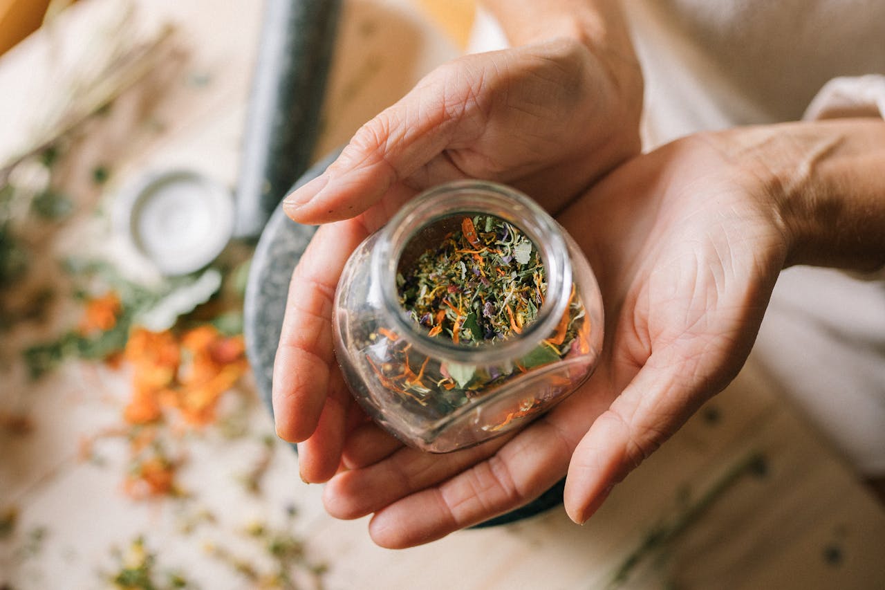 about-03 Close-up of hands holding a glass jar filled with colorful dried herbs.